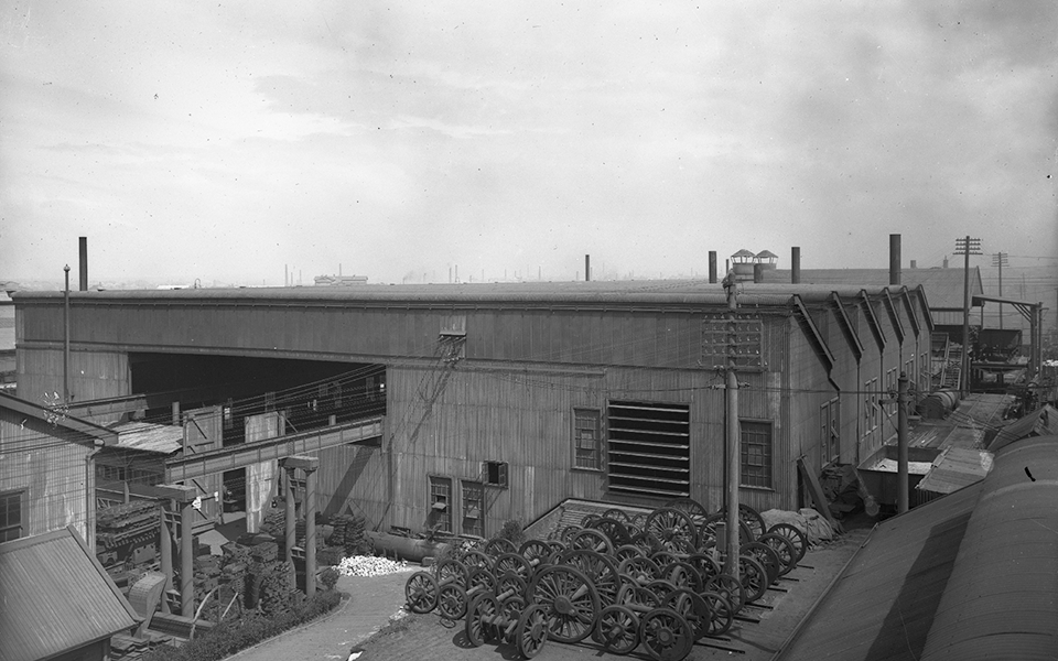 Plumes of ash and smoke from metal working covers the corrugated-iron sawtooth roofed foundry in a haze. The northern side of the foundry opened towards the foundry pattern shop and store, partially visible in the left of the image. 
